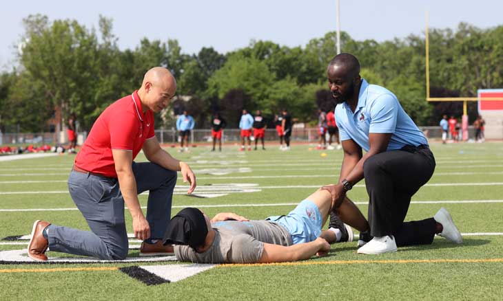 Two sports medicine physicians treat a player on a football field.