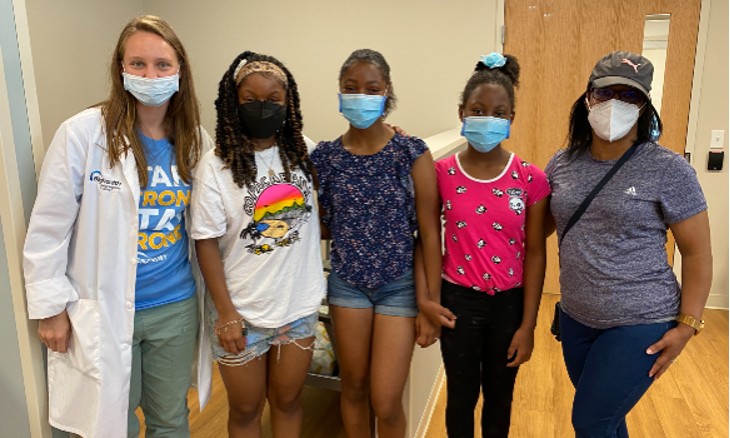 A physician resident poses with a mother and her three daughters who received free sports physicals.